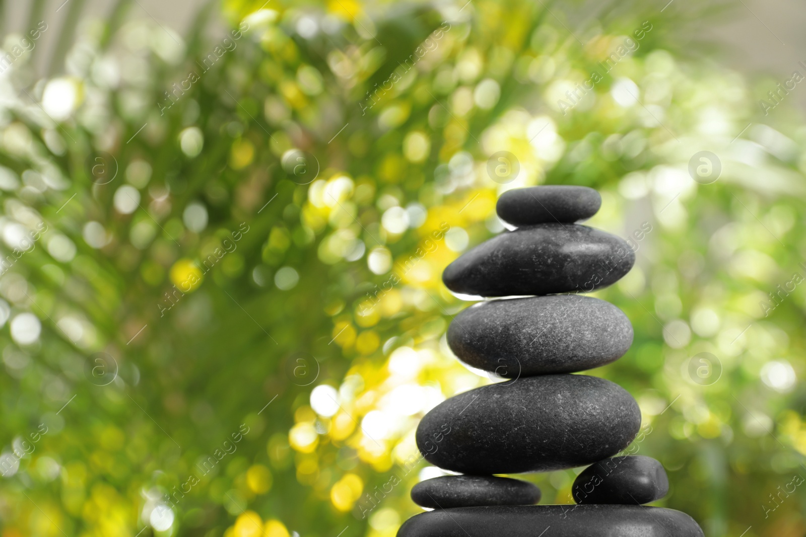 Photo of Stack of stones and blurred green leaves on background, space for text. Zen concept