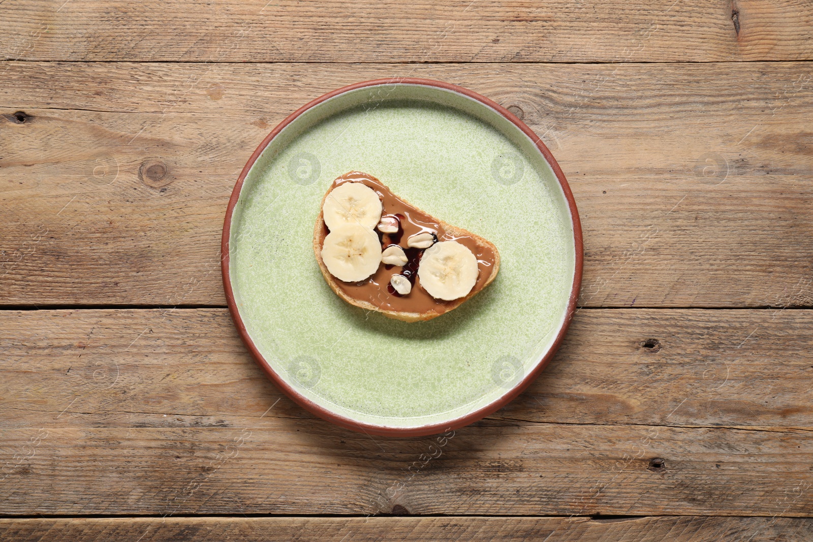 Photo of Toast with tasty nut butter, banana slices and peanuts on wooden table, top view