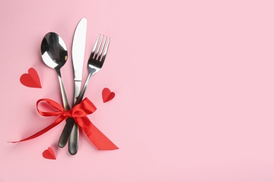 Photo of Beautiful cutlery set, hearts and red bow on pink background, flat lay with space for text. Valentine's Day dinner