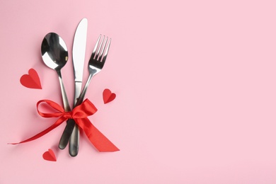 Beautiful cutlery set, hearts and red bow on pink background, flat lay with space for text. Valentine's Day dinner