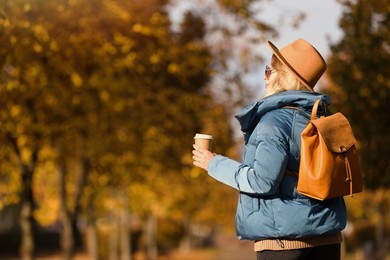 Photo of Young woman with stylish backpack and hot drink on autumn day, space for text