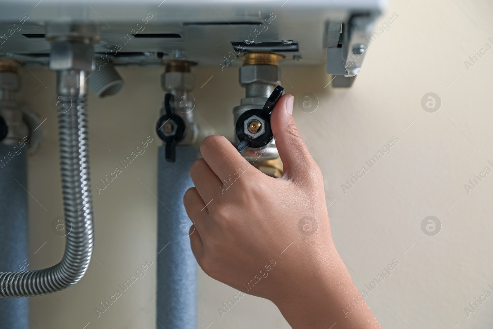 Photo of Woman turning on valve of gas boiler, closeup