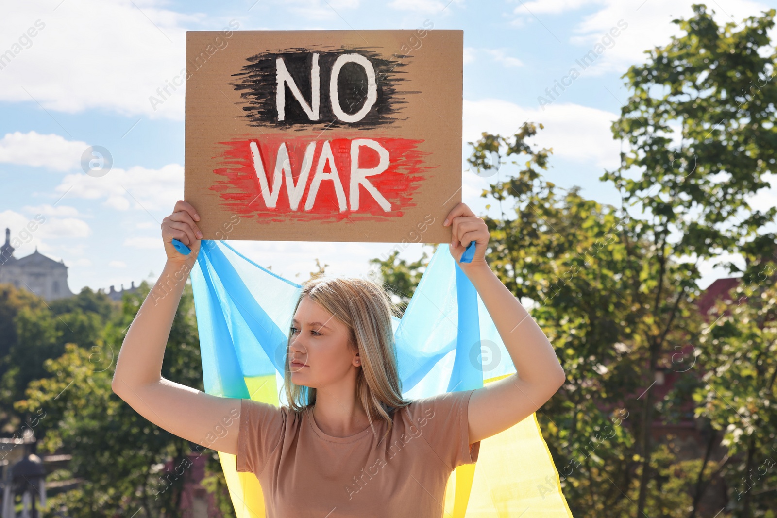 Photo of Sad woman holding poster with words No War and Ukrainian flag outdoors