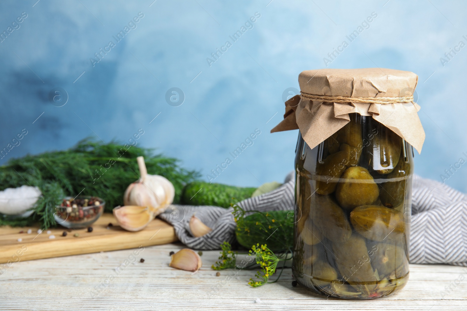 Photo of Jar with pickled cucumbers on white wooden table against blue background