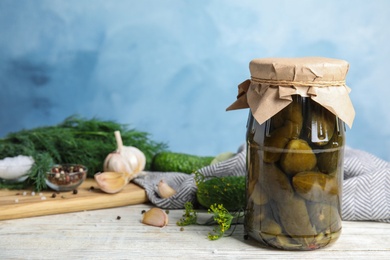 Photo of Jar with pickled cucumbers on white wooden table against blue background