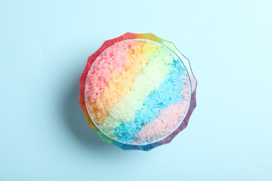 Rainbow shaving ice in glass dessert bowl on light blue background, top view