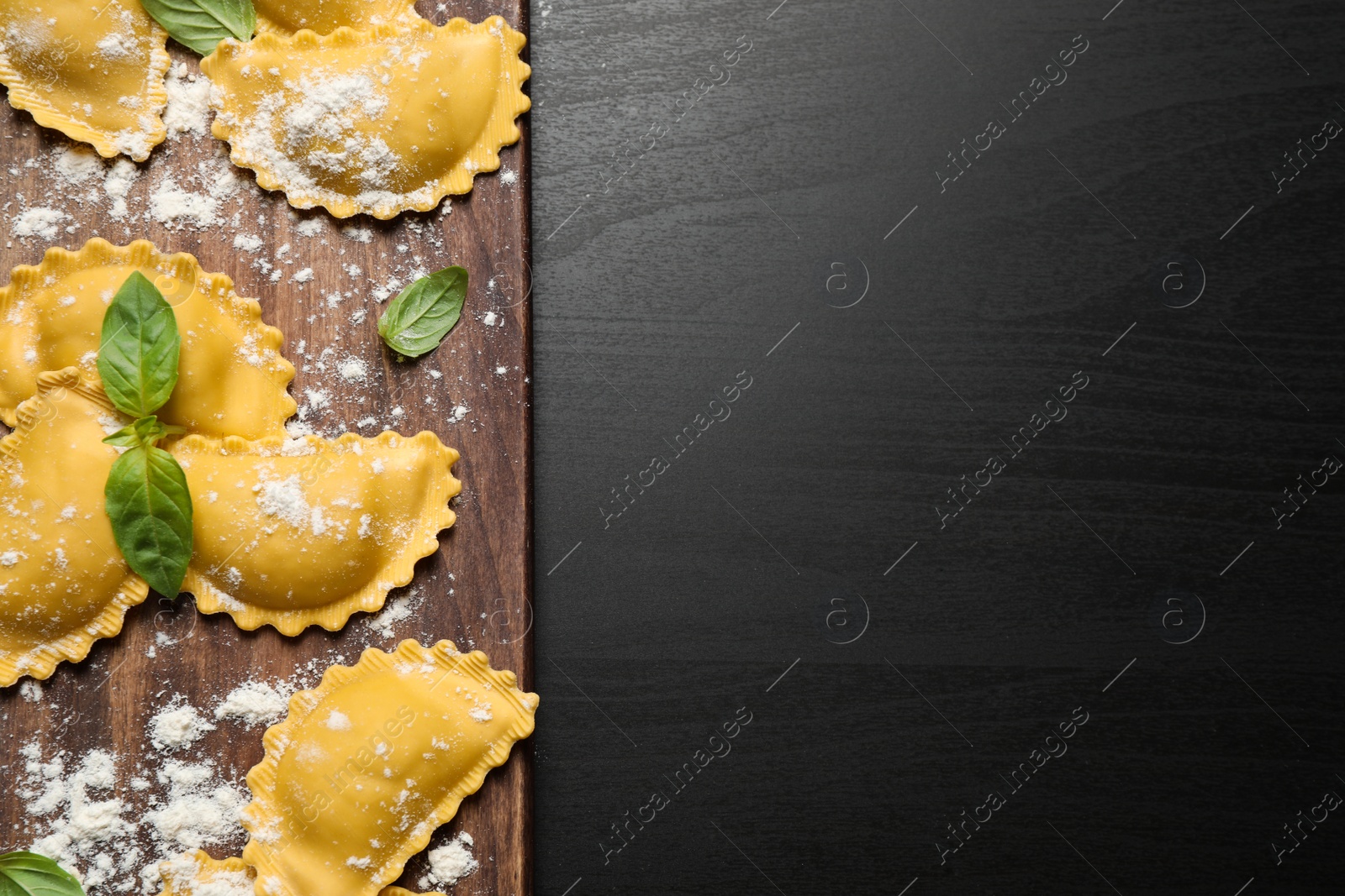 Photo of Raw ravioli with basil on black wooden table, flat lay and space for text. Italian pasta