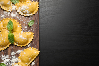 Raw ravioli with basil on black wooden table, flat lay and space for text. Italian pasta