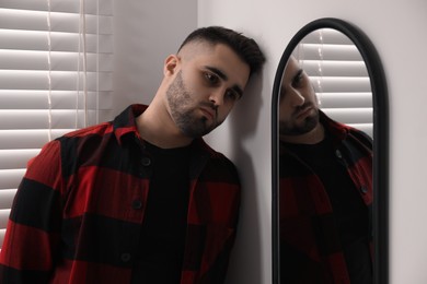 Sad young man near mirror at home