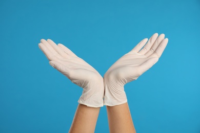 Doctor wearing medical gloves on light blue background, closeup