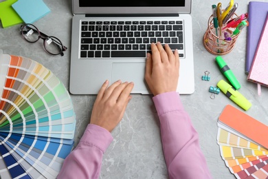 Woman working with laptop and palette samples at grey table, top view