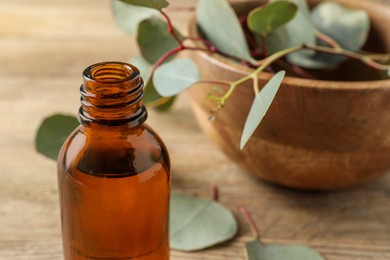 Photo of Bottle of eucalyptus essential oil and leaves on wooden table, closeup. Space for text