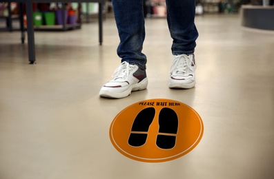 Image of Keep social distance as preventive measure during coronavirus outbreak. Orange warning sign on floor in front of man, closeup