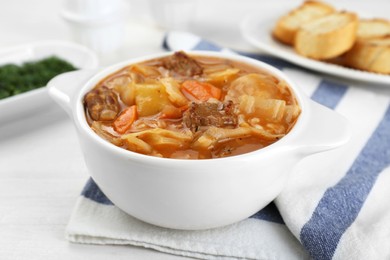 Tasty cabbage soup with meat and carrot on white wooden table, closeup