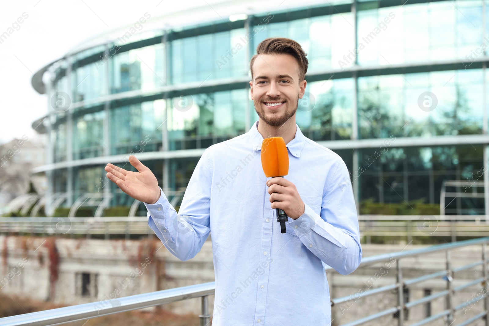 Photo of Young male journalist with microphone working on city street