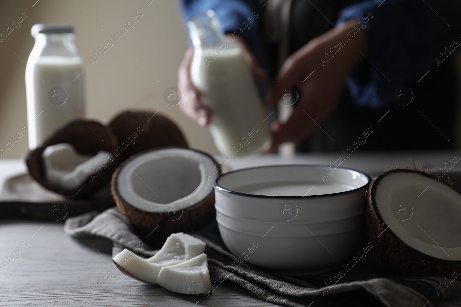 Photo of Bowl of coconut milk and nuts on white wooden table, selective focus. Space for text
