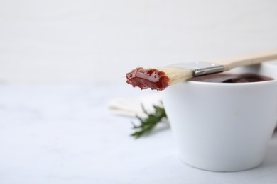 Photo of Marinade in bowl and basting brush on white table, closeup. Space for text