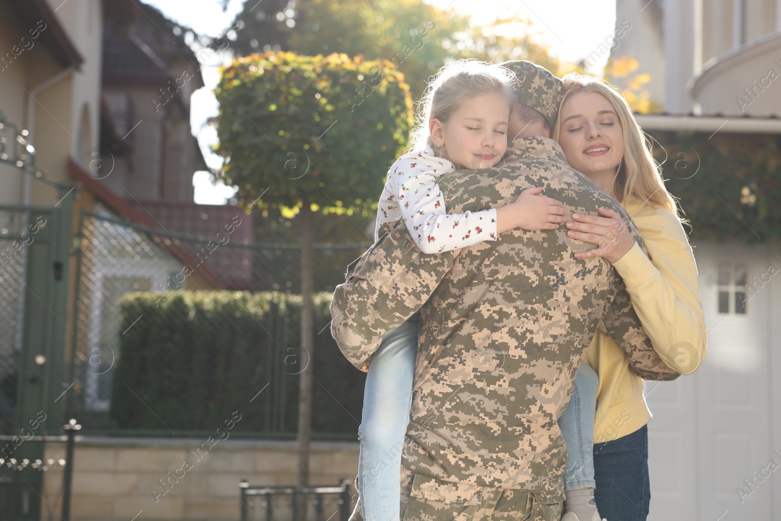 Photo of Daughter and wife hugging soldier in Ukrainian military uniform outdoors, space for text. Family reunion