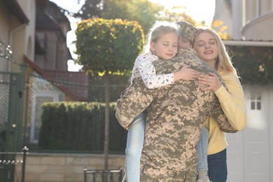 Photo of Daughter and wife hugging soldier in Ukrainian military uniform outdoors, space for text. Family reunion