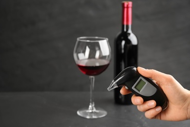 Woman holding modern breathalyzer near black table with wine, closeup. Space for text