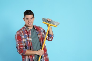 Man with yellow broom on light blue background, space for text