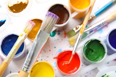 Jars with color paints and brushes on table, top view