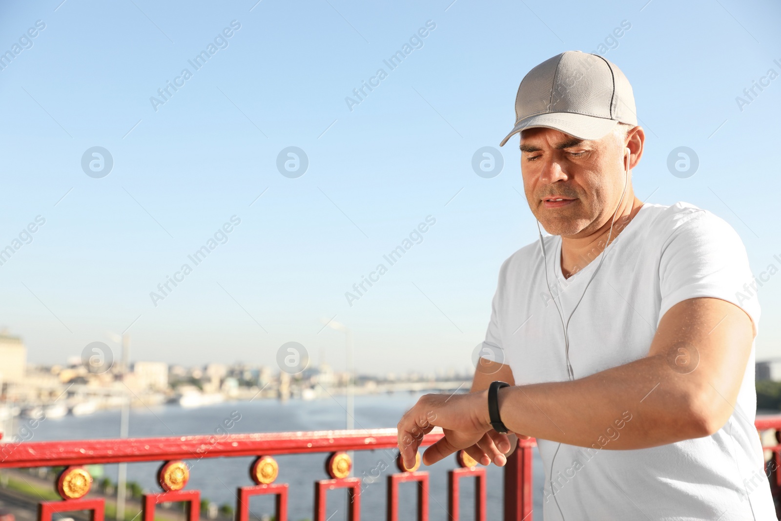 Photo of Handsome mature man looking at fitness tracker on bridge, space for text. Healthy lifestyle