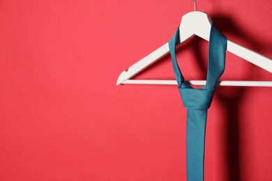 Photo of Hanger with dark turquoise tie on red background. Space for text