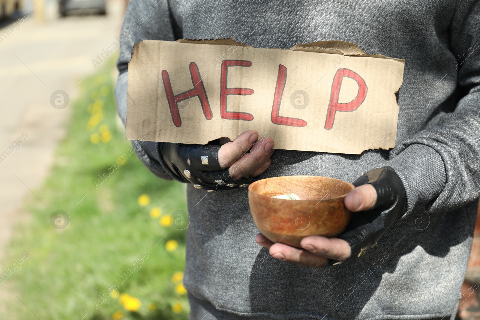 Photo of Poor homeless man holding help sign and bowl with donations outdoors, closeup