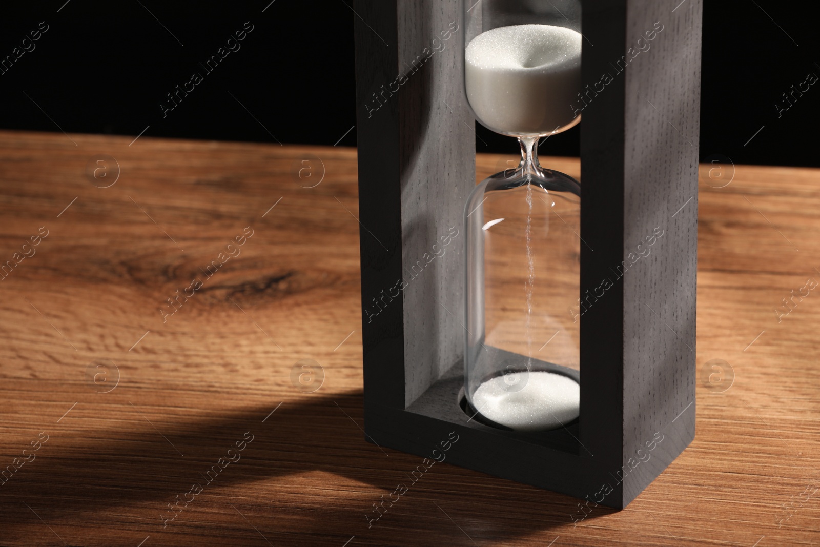 Photo of Hourglass with white flowing sand on wooden table, closeup. Space for text