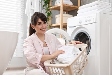 Photo of Happy young housewife with laundry near washing machine at home