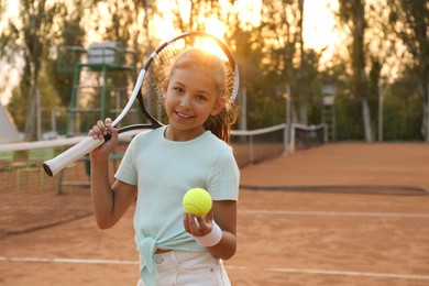 Photo of Cute little girl with tennis racket and ball on court outdoors