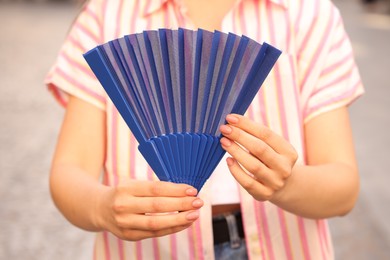 Photo of Woman with blue hand fan outdoors, closeup