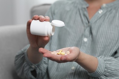 Photo of Woman pouring antidepressants from bottle on blurred background, closeup