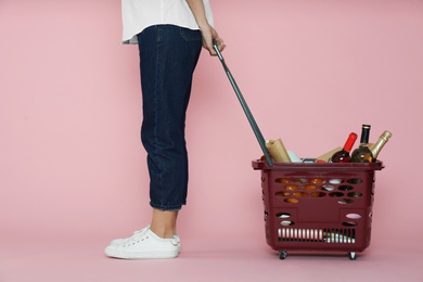 Woman with shopping basket full of different products on pink background, closeup