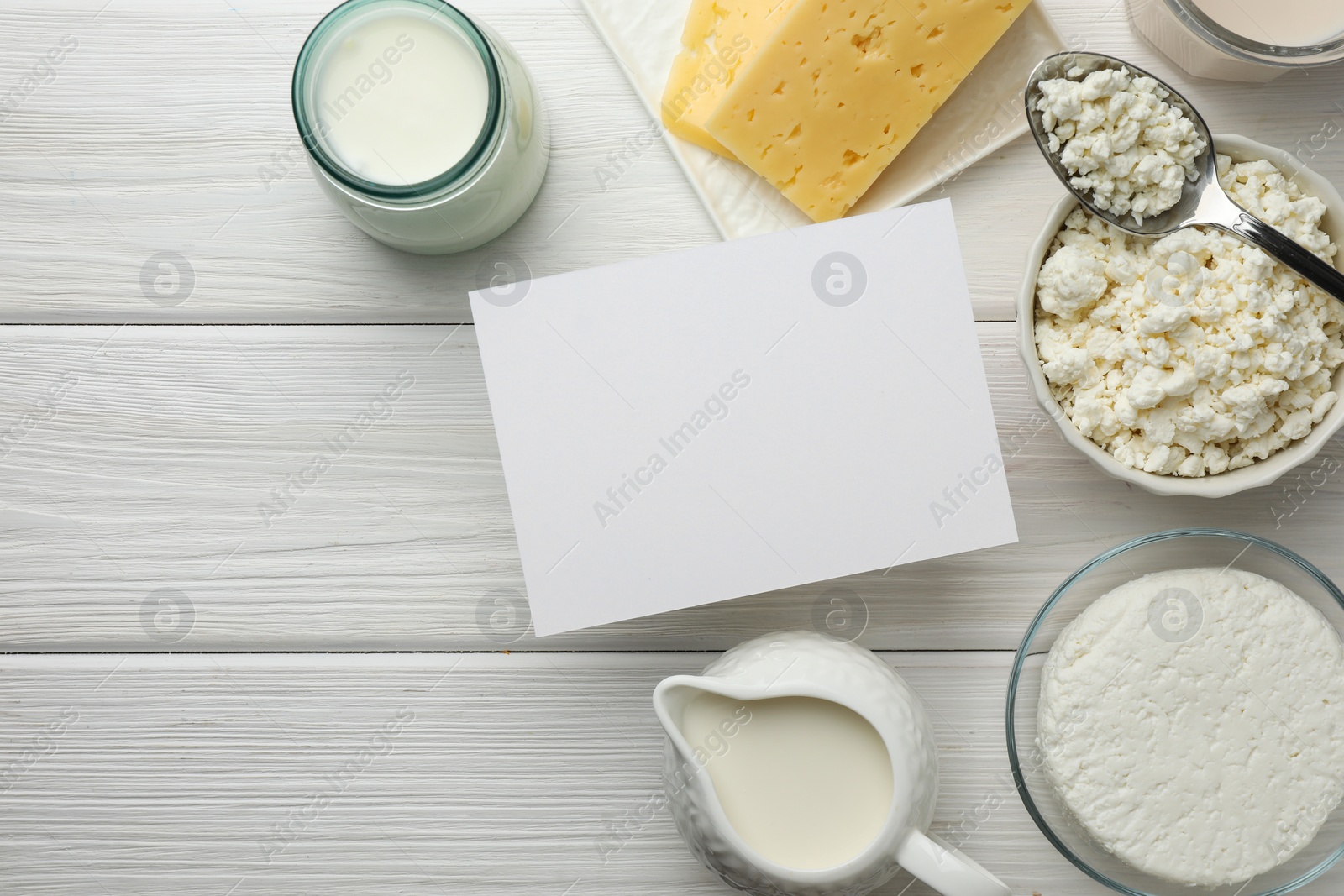 Photo of Dairy products and blank card on white wooden table, flat lay. Space for text
