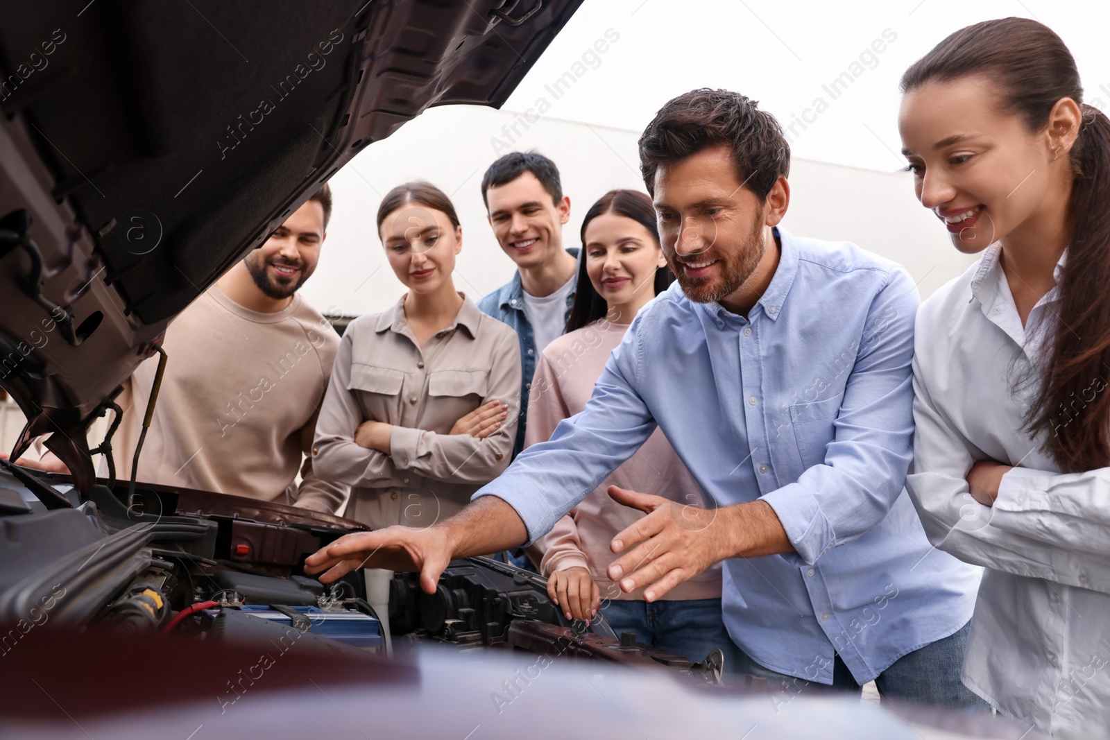 Photo of Driving school. Teacher explaining car engine to group outdoors