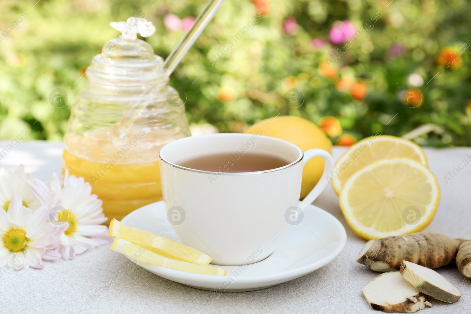 Photo of Cup of delicious tea with honey, lemon and ginger on white table outdoors