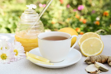 Photo of Cup of delicious tea with honey, lemon and ginger on white table outdoors