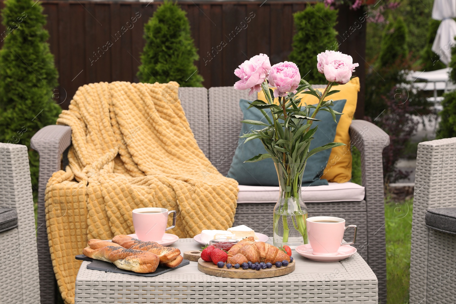 Photo of Morning drink, pastry, berries, cheese and vase with flowers on rattan table. Summer breakfast outdoors