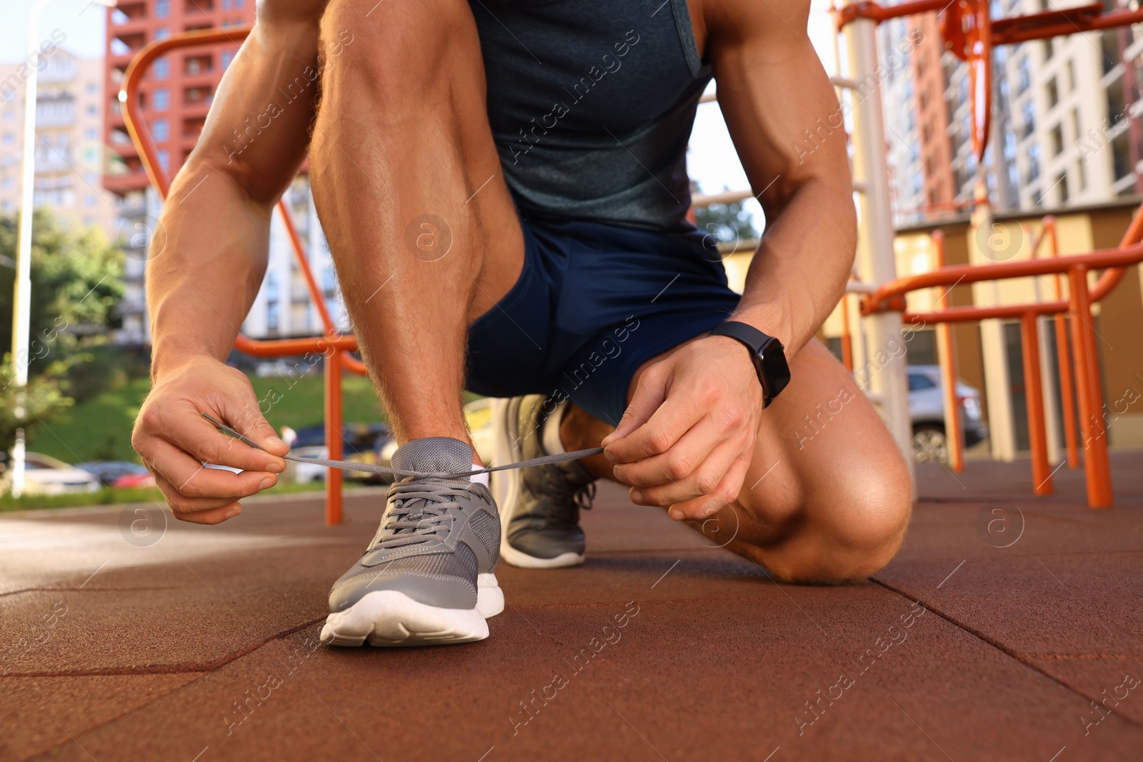 Photo of Man tying shoelaces before training at outdoor gym, closeup