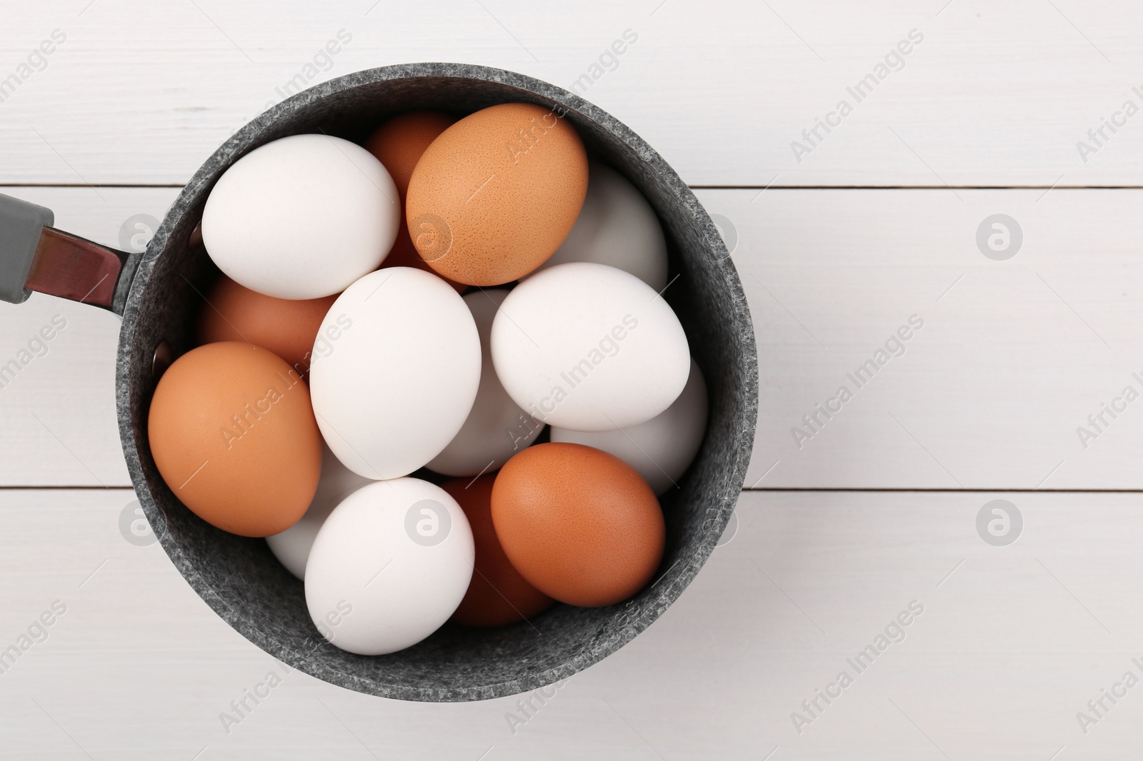 Photo of Unpeeled boiled eggs in saucepan on white wooden table, top view. Space for text