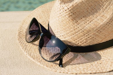 Stylish hat and sunglasses near outdoor swimming pool on sunny day, closeup