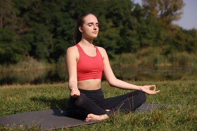 Beautiful woman practicing yoga on mat outdoors. Lotus pose