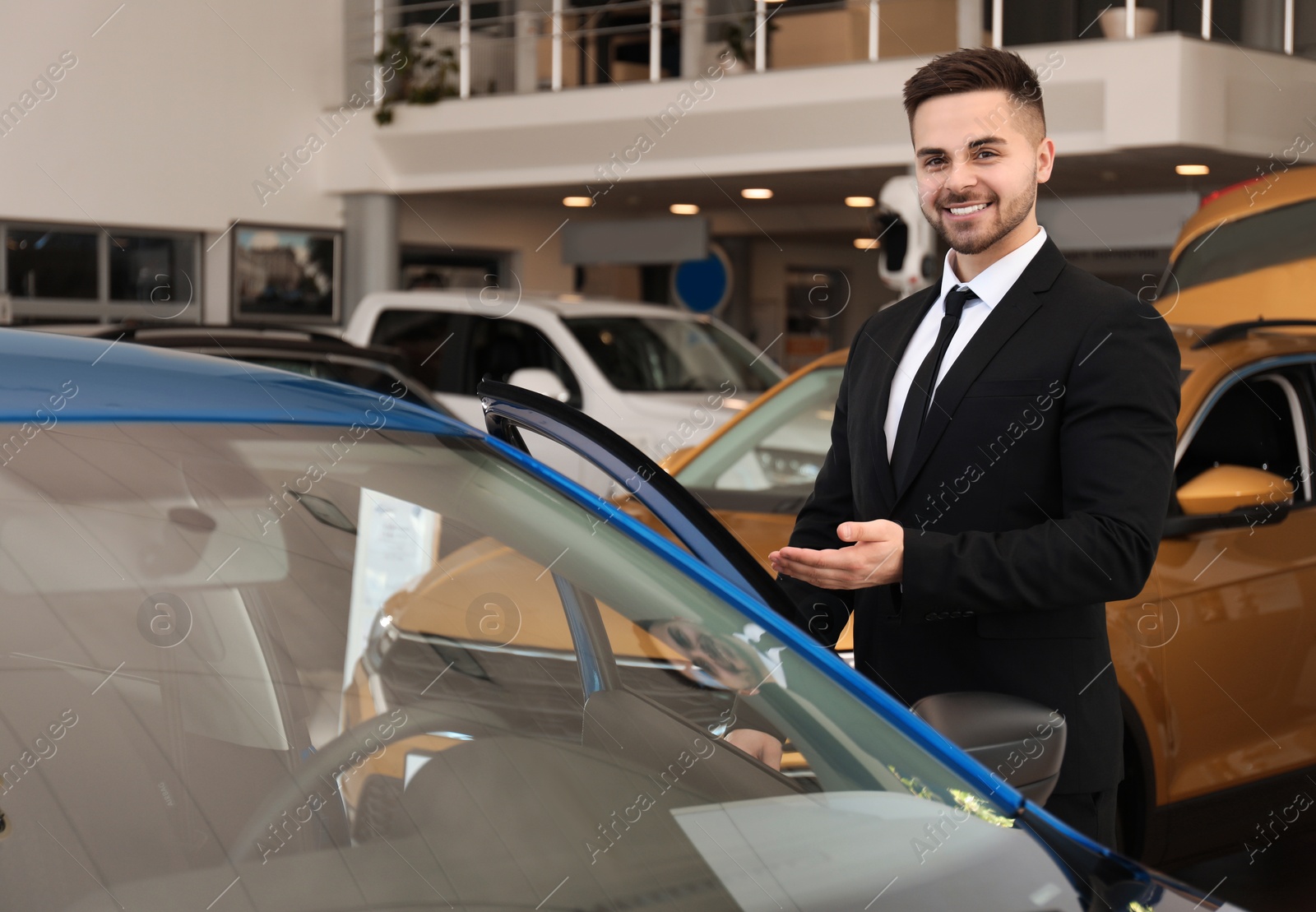 Photo of Young salesman near new car in dealership