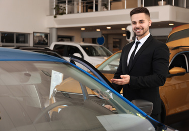 Photo of Young salesman near new car in dealership