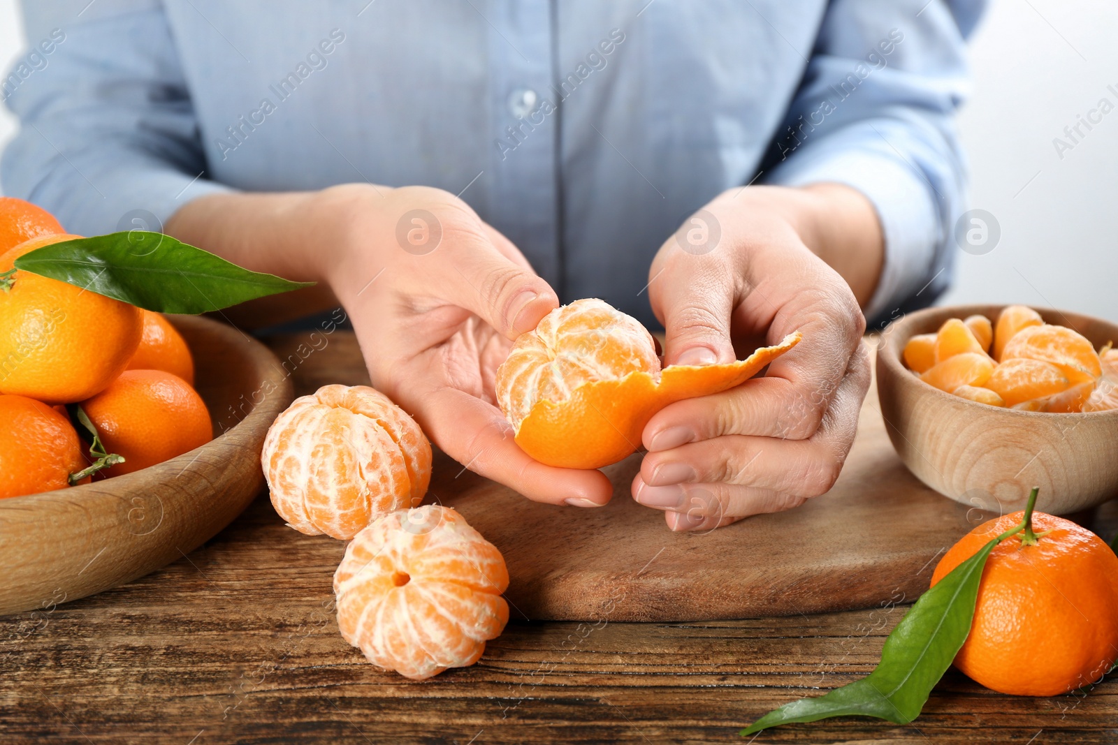 Photo of Woman peeling fresh ripe tangerine at wooden table, closeup