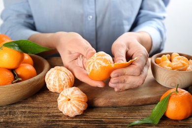 Photo of Woman peeling fresh ripe tangerine at wooden table, closeup