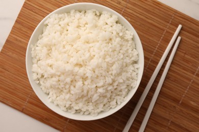 Bowl with delicious rice and chopsticks on white table, flat lay