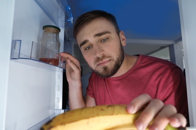 Man looking into refrigerator and choosing products in kitchen